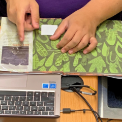 An RFID tagging technician works at a mobile workstation cart to place an RFID tag into a book.