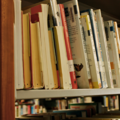A bookshelf has books, some laid on their spine with a single black sharpie dot at the top of the book block, in mid-processing. These methods assist technicians with quality assurance.