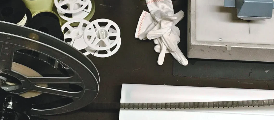 Reels, gloves, and microfilm are shown on a table, the film extended over a lightbox.