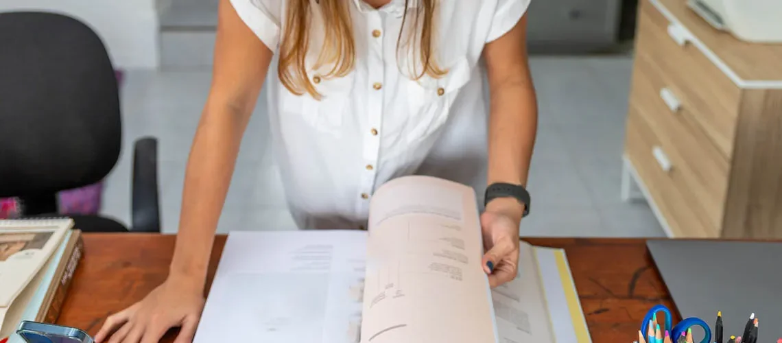 woman standing in front of her desk with a large open book turning pages. Home office concept